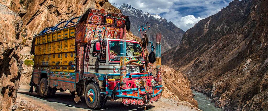 A colorful truck drives on a rural road through the Pakistan mountains
